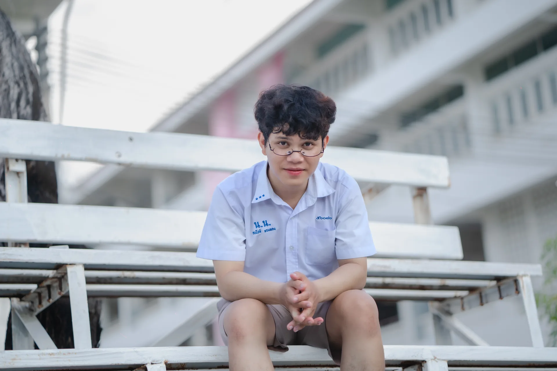 Thanachot Phomthong sitting on a white bench outside a school building